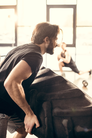 side view of athletic young man lifting tire in gymの写真素材