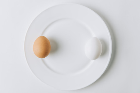 white and brown eggs laying on plate on white backgroundの写真素材