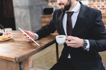 cropped image of loner businessman looking at tablet and holding cup of coffee at kitchenの写真素材