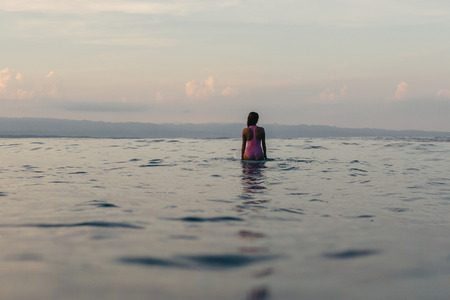 back view of silhouette of female surfer sitting on surfboard in waterの写真素材