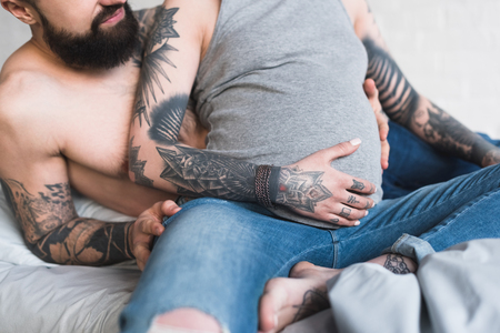cropped image of boyfriend hugging pregnant tattooed girlfriend on bedの写真素材
