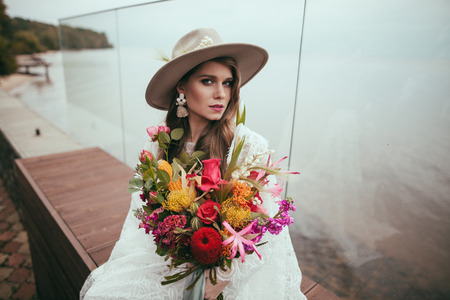 attractive bride in bohemian wedding dress and hat with bouquetの写真素材
