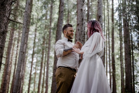 low angle view of beautiful young bride and groom holding hands and looking at each other in alpine forestの写真素材