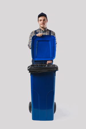 portrait of young cleaner in uniform with trash bin isolated on greyの写真素材