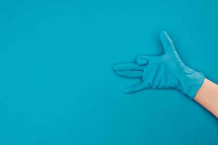 cropped image of woman showing sign with hand in rubber protective glove isolated on blueの写真素材