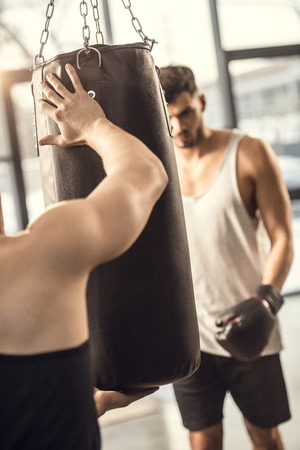 selective focus of trainer holding punching bag while boxer training in gymの写真素材
