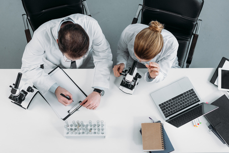 overhead view of scientific researchers in white coats working together at workplace in laboratoryの写真素材