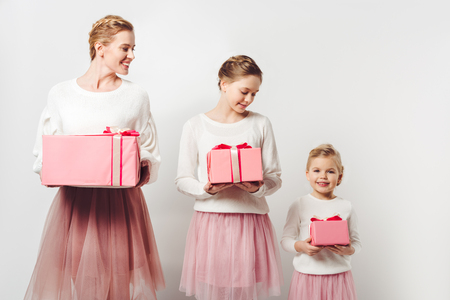 smiling mother and little daughters in similar pink tutu tulle skirts with wrapped gifts isolated on greyの写真素材