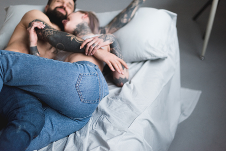 tattooed shirtless couple hugging on bedの写真素材