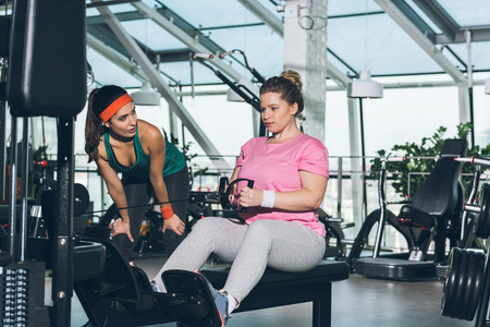 overweight woman working out on training apparatus while trainer watching herの写真素材