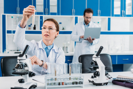 selective focus of female scientist looking at tube with reagent in hand with colleague behind in labの写真素材