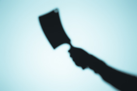 scary blurry shadow of person holding meat knife on blueの写真素材