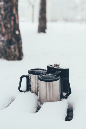 close up view of thermocups and flask in snow on winter day in forestの写真素材