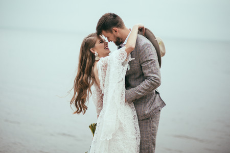 cheerful bride and groom in boho style hugging at lakeの写真素材