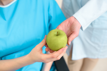 cropped shot of doctor passing green apple to pregnant woman on wheelchairの写真素材