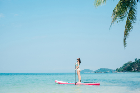 young girl on stand up paddle board on sea at tropical resortの写真素材