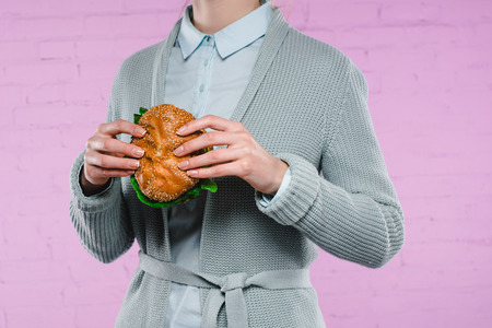cropped shot of woman in sweater and shirt holding tasty burgerの写真素材