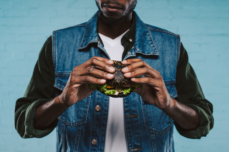 cropped shot of african american man holding tasty black burgerの写真素材