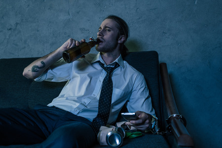 young alcohol addicted man in white shirt watching tv and drinking beer after work