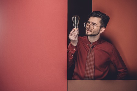 Creative businessman looking at bulb by red paper walls isolated on blackの写真素材