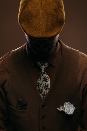 Man wearing corduroy vest and flat cap isolated on brownの写真素材