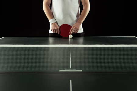 partial view of tennis player with racket standing at tennis table isolated on blackの写真素材