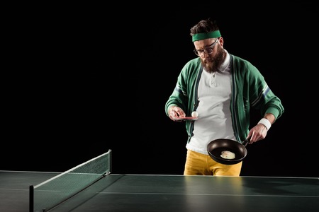 bearded sportsman with tennis equipment and egg on frying pan isolated on blackの写真素材