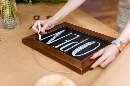 close-up partial view of young florist writing word open with chalk on board