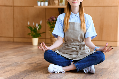 cropped shot of smiling young florist in apron sitting in lotus position on floorの写真素材
