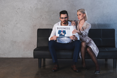 sexy girl in stockings flirting with handsome businessman reading newspaper on couchの写真素材