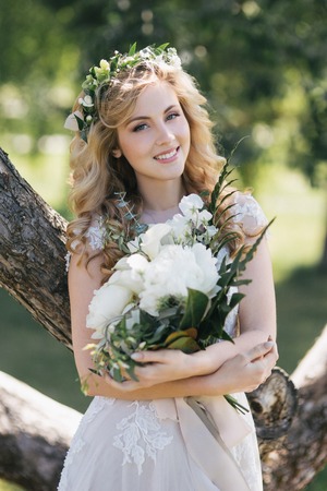 beautiful young bride holding wedding bouquet and smiling at cameraの写真素材