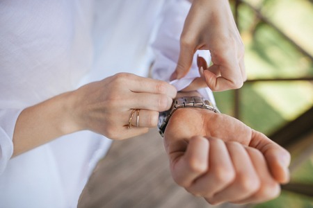 close-up partial view of woman buttoning shirt to groom before weddingの写真素材