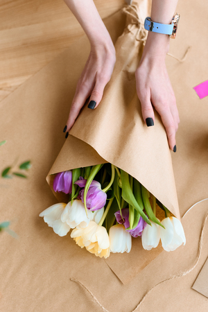 cropped shot of young florist arranging beautiful bouquet of tulips in craft paperの写真素材