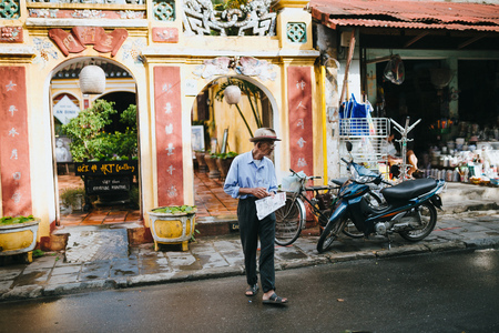 HOI AN, VIETNAM - 03 JANUARY, 2018: senior vietnamese man with newspaper walking on street in Hoi An, Vietnamのeditorial素材
