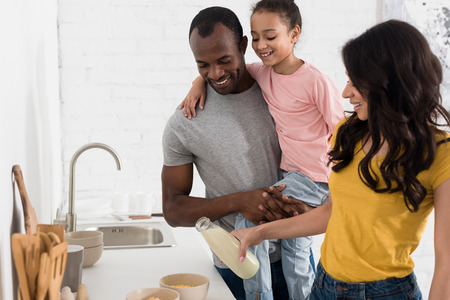 happy young family pouring milk into cereal breakfast at kitchenの写真素材