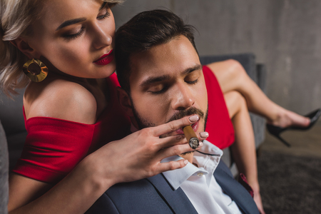 close-up view of sexy girl in red dress holding cigar while boyfriend smoking itの写真素材