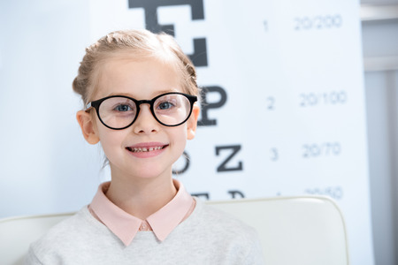 adorable child looking at camera in glasses at oculist consulting room
