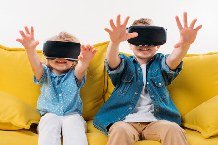 siblings gesturing and using virtual reality headset while sitting on sofa