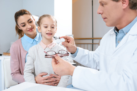 mother and daughter visiting optometrist and choosing eyeglasses or contact lenses in clinicの写真素材