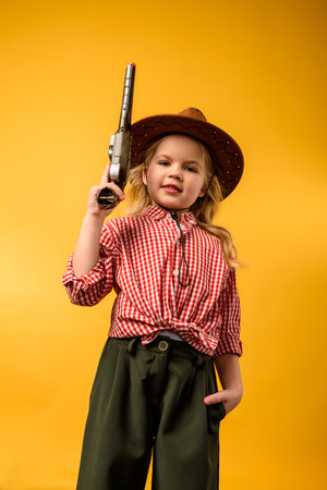 stylish cowgirl in hat with gun, isolated on yellowの写真素材