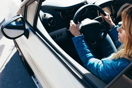 Side view of young woman with hands on steering wheel driving carの写真素材