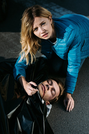 High angle view of young woman crying about dead body and looking at camera on roadの写真素材