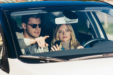 Man with smartphone showing direction to girlfriend in car