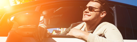 Smiling young man leaning out car window of driving automobile