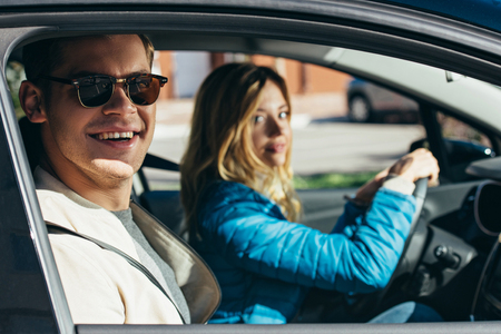 Young woman driving car with boyfriend in sunglasses near by, traveling conceptの写真素材
