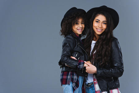 Young embracing mother and daughter in leather jackets isolated on greyの写真素材