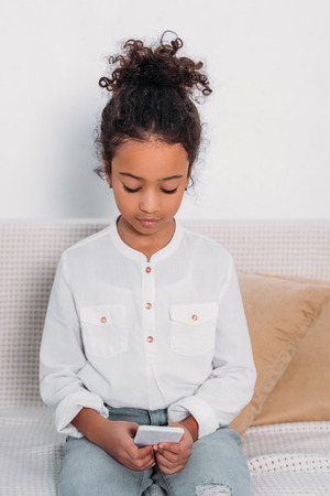 adorable african american kid using smartphone on sofaの写真素材