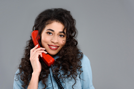 Happy young woman talking by vintage red phone isolated on greyの写真素材