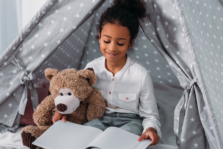 African american kid reading book and hugging teddy bearの写真素材