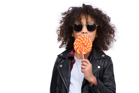 Beautiful little child in leather jacket and sunglasses eating lollipop isolated on whiteの写真素材
